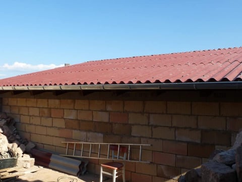 Neu verlegtes Dach mit roten Faserzement Wellplatten, Baustelle im Vordergrund