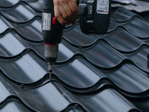 Handwerker montiert schwarzes Pfannenblechdach mit Akkuschrauber – professionelle und präzise Arbeit