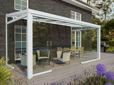 Moderne Terrassenüberdachung mit Glasschiebewänden, integriert in eine idyllische Gartenlandschaft mit Sitzgruppe