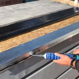 Montage des schwarzen Anschlussklebers Flex auf einem Dachblech mit einer Kartuschenpistole