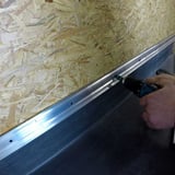 Montage einer Metallschiene mit Akkuschrauber ueber dem schwarzen Anschlusskleber Flex auf Dachfolie