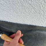 Detailansicht der Verlegung des grauen doppelseitigen Dichtbands an einer weissen Wand