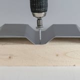 Montage einer anthrazitgrauen Trapezblech-Tiefsicke mit Edelstahlschraube auf Holz, Bohrmaschine ansetzend