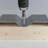 Montage einer Edelstahlschraube in die Tiefsicke einer Trapezblechplatte auf Holz, Bohrer angesetzt