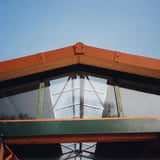 Endstueck in Ziegelrot an der Dachspitze eines Holzunterstands, von unten gegen blauen Himmel