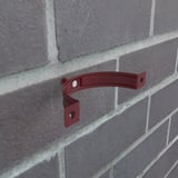 Kirschrote Fallrohrschelle aus Stahl, Polyurethan beschichtet, an einer Ziegelwand montiert