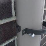 Fallrohrschelle aus anthrazitgrauem Stahl um ein helles Fallrohr an Ziegelwand