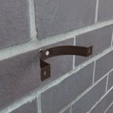 Montierte schokoladenbraune Fallrohrschelle aus Stahl an einer Ziegelwand, ohne Fallrohr