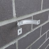 Einzelne verzinkte Fallrohrschelle an einer dunklen Ziegelwand montiert, ohne Fallrohr