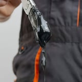 Detailaufnahme von dunklem Flüssigkunststoff, der von einem Pinsel tropft