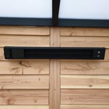 Schwarze Aluminium-Heizung an einer vertäfelten Holzwand, mittig montiert