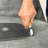 Hand rollt mit Metall-Eckenroller eine dunkle Dachbahn an einer Ecke fest