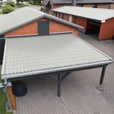 Carport mit Dach aus Pfannenblech in Weißaluminium, an einem Ziegelhaus