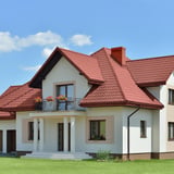 Pfannenblech Szafir 350/15 in Rotbraun auf dem Dach eines weissen Einfamilienhauses mit Balkon