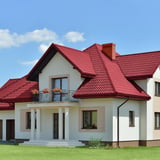 Haus mit weinrotem Pfannenblech Szafir 350/15 Dach, Vorderansicht mit Balkon und Gauben