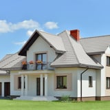 Einfamilienhaus mit Dach aus Pfannenblech Szafir 350/15 Graualuminium, helle Fassade, rote Dachrinne