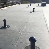 Mehrere schwarze EPDM Rohrmanschetten auf einem Flachdach mit Entlueftungsrohren, von oben gesehen