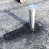 Detailansicht einer schwarzen EPDM Rohrmanschette um ein silbernes Entlueftungsrohr auf einem Flachdach