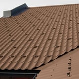Dach mit dunkelbraunen Dachpfannenprofilplatten und montierten Schneefangbügeln, Verlegung