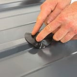 Hände drücken einen schwarzen EPDM Schrauben Reparaturflicken auf ein graues Trapezblech