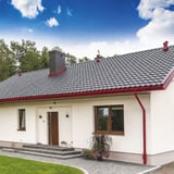 Weisses Haus mit kirschroter Niagara Stahl Dachrinne und Fallrohr, komplett am Dach montiert