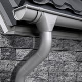 Stahl Dachrinne in Graualuminium (RAL 9007) am Dach eines Hauses montiert, mit Fallrohr und Bogen
