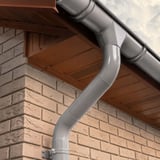 Stahl Dachrinne in Graualuminium (RAL 9007) mit Fallrohr und Schelle an einer Ziegelwand