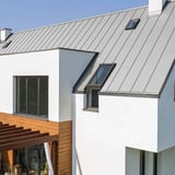 Stehfalzblech PD-510-S Flach Lichtgrau auf einem Hausdach mit Dachfenstern und Holzfassade