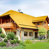 Wohnhaus mit rapsgelbem Stehfalzdach und Holzbalkon, umgeben von Gartenlandschaft