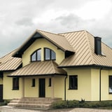 Haus mit Stehfalzblech PD-510-S Flach in Hellelfenbein RAL 1015 auf dem Dach, mit Gauben und Schornstein
