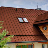 Nahaufnahme des ziegelroten Stehfalzblechdachs PD-510-S Mikro mit Dachfenstern und Holzelementen