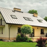 Stehfalzblech PD-510-S Mikro Reinweiß auf einem Wohnhaus mit Garten und mehreren Dachfenstern