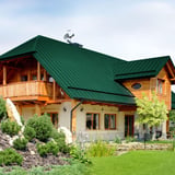 Stehfalzblech PD-510-S Mikro Gruen auf einem Wohnhaus mit Holzfassade und Dachschmuck