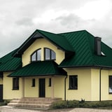 Stehfalzblech PD-510-S Mikro Gruen auf einem Wohnhaus mit gelber Fassade und dunklen Fenstern