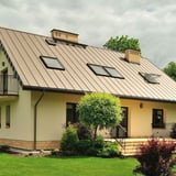 Stehfalzblech PD-510-S Mikro Hellelfenbein RAL 1015 auf einem Hausdach mit mehreren Dachfenstern