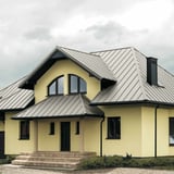 Stehfalzblech PD-510-S Mikro, Grauweiß RAL 9002, auf einem Hausdach mit gelber Fassade