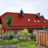 Haus mit Dach aus korallenrotem Stehfalzblech PD-510-S, mit Dachfenstern und Schornstein