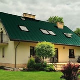 Stehfalzblech PD-510-S Nano in Grün auf einem Wohnhaus mit mehreren Dachfenstern und Schornsteinen, Verlegung am Dach