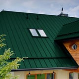 Stehfalzblech PD-510-S Nano in Grün auf einem Wohnhaus mit Holzfassade und Dachfenstern, Verlegung am Dach