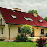 Stehfalzblech PD-510-S Kirschrot auf einem Wohnhaus mit Dachfenstern und Schornsteinen, Verlegung