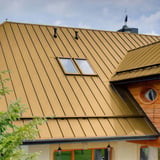Stehfalzblech PD-510-S Sandgelb auf einem Wohnhaus mit zwei Dachfenstern und Holzelementen
