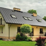 Stehfalzblech PD-510-S Weißaluminium auf einem Hausdach mit mehreren Dachfenstern und Schornsteinen