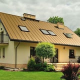 Stehfalzblech PD-510-S Trapezblech sandgelb auf einem Wohnhaus mit mehreren Dachfenstern