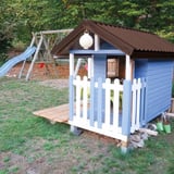 Trapezblech 20/1100 schokoladenbraun als Dach auf einem blauen Kinderspielhaus mit Rutsche im Hintergrund