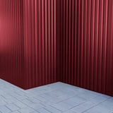 Ecke einer weinroten Trapezblech 20/1100 Wand, vertikal verlegt, mit Pflastersteinen