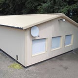 Trapezblech 35/207 Reinweiß auf einem beigefarbenen Gebäude mit Fenstern und Satellitenschüssel