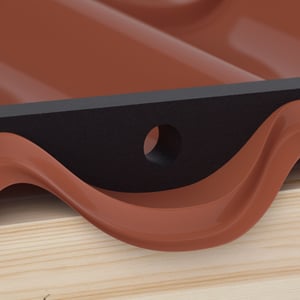 Profilfüller aus schwarzem Schaumstoff mit Belüftungsloch, unter einem roten Dachblech auf Holzlatten