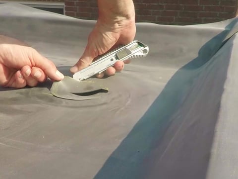 Eine Person führt eine Reparatur an einer EPDM-Dachfolie durch, indem sie mit einem Cutter ein Stück beschädigter Folie ausschneidet
