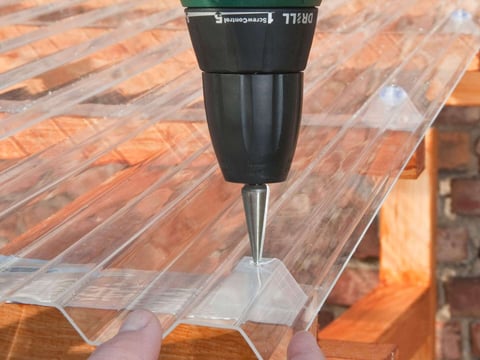 Handwerkliche Montage von durchsichtigen Wellplatten mit einem Akkubohrschrauber auf einem Holzdachstuhl, präzise und effiziente Heimwerkerarbeit