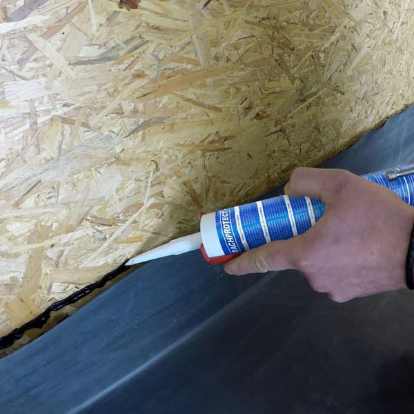 Detailansicht der Anwendung von schwarzem Anschlusskleber Flex auf einer OSB-Platte mit Dachfolie